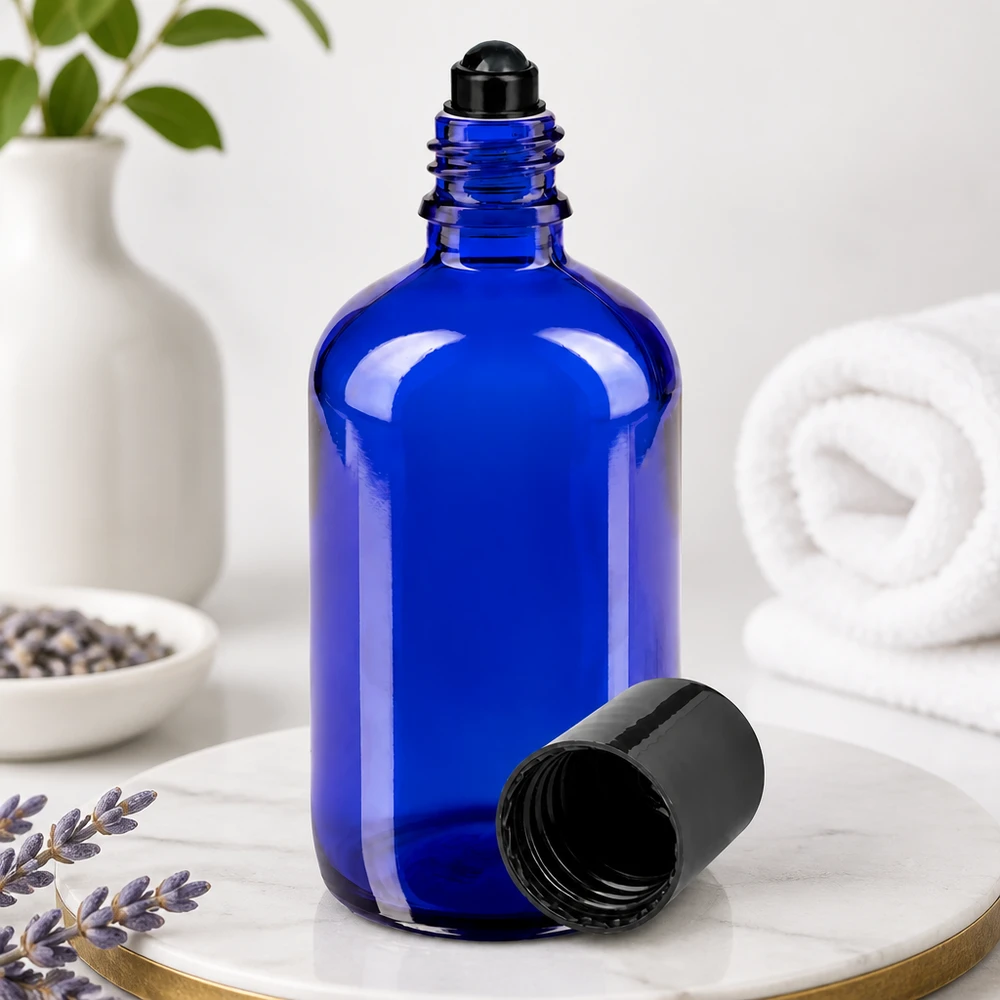 Botella de farmacia azul 100ml roll-on cap negro Botella de cristal azul de 100 ml con bola rodante negra y la tapa retirada, sobre una superficie de mármol
