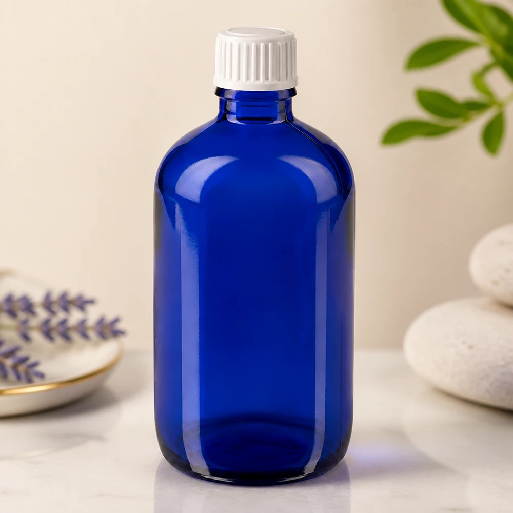 Botella de farmacia azul 100ml tapón rosca blanco estándar Botella de cristal azul de 100 ml con tapón de seguridad para niños de color blanco sobre una superficie de mármol, junto a la lavanda