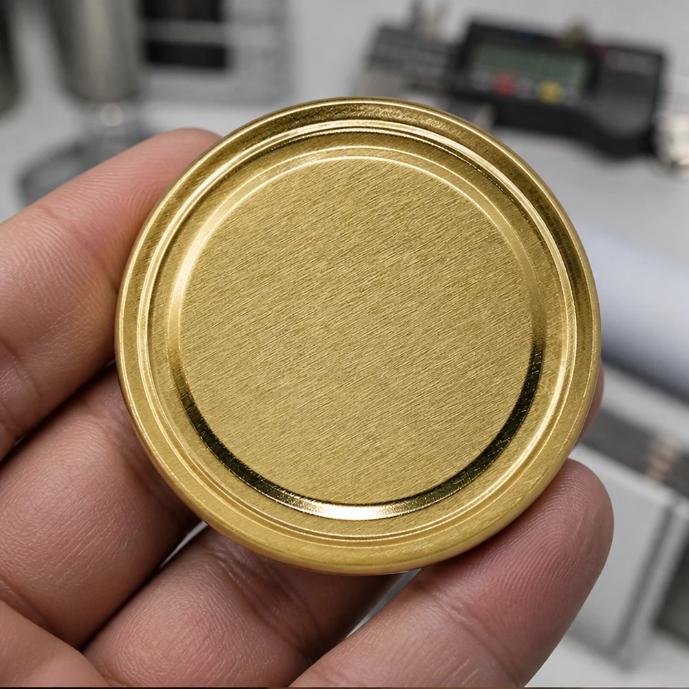 Tapa BasicSeal de 63 mm, color dorado (TO63) UNiTWIST Primer plano de una tapa dorada para tarros TO63 de 63 mm, modelo BasicSeal UniTwist, en la mano de un hombre