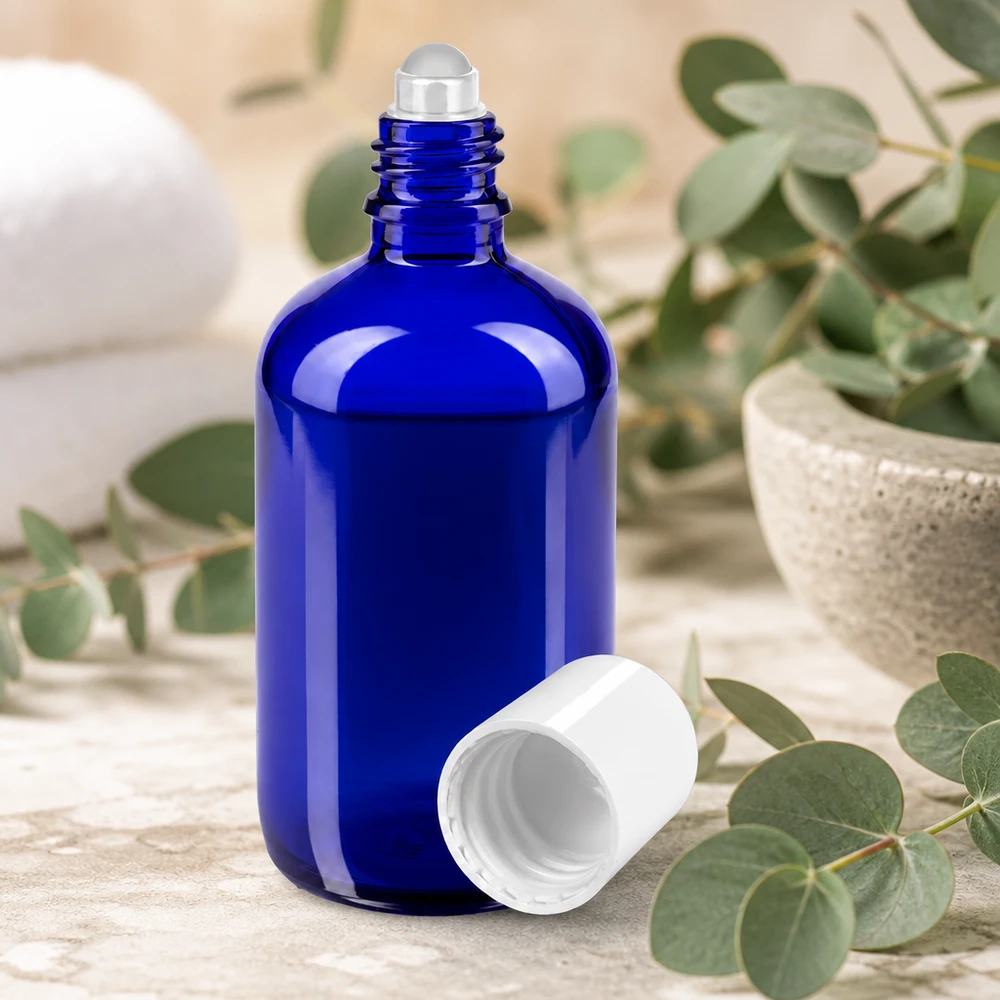 Frasco roll-on de 100 ml de color azul con bola de acero y tapón blanco entre ramas de eucalipto
