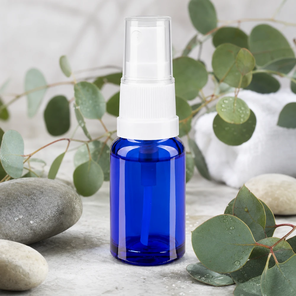 Frasco de 10 ml de cristal de farmacia azul cobalto con un pulverizador blanco rodeado de ramitas de eucalipto