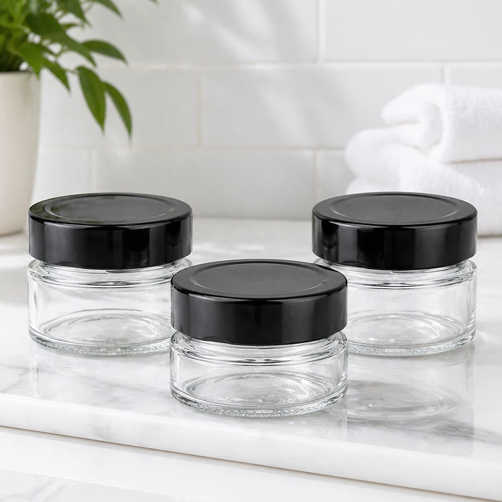 Tres tarros redondos de 80 ml con tapas negras BasicSeal UNiTWIST sobre encimera de mármol blanco Ambiente de baño vacío