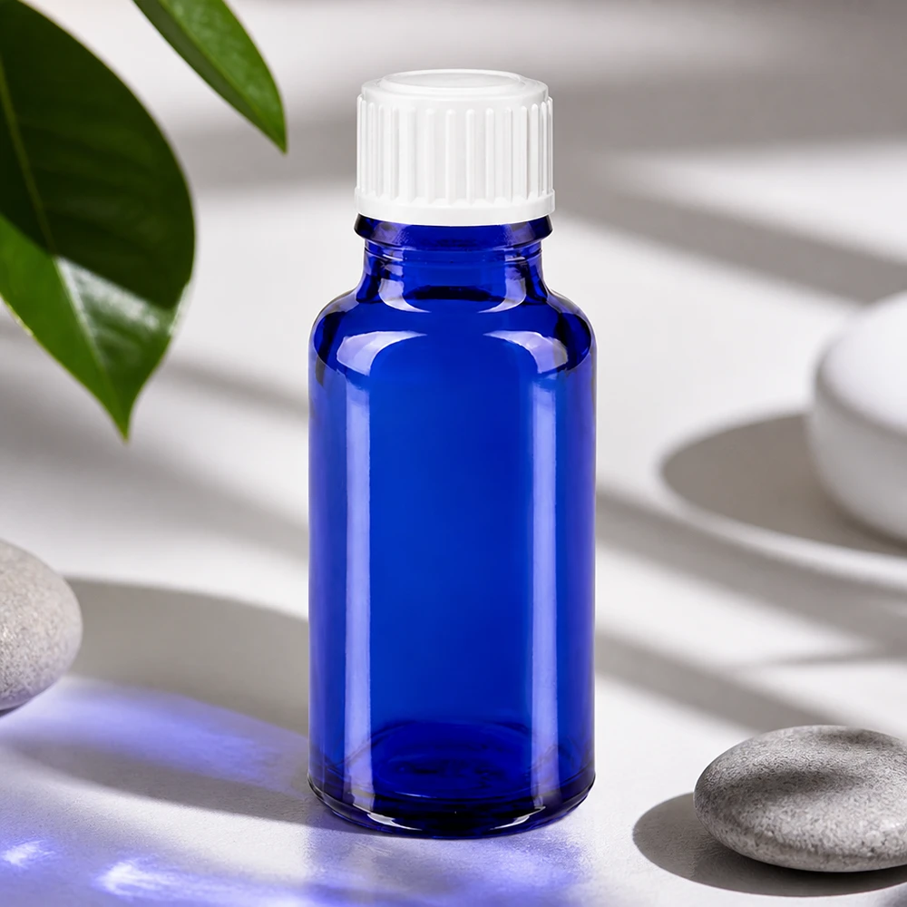 Frasco de cristal azul de 20 ml con tapón blanco junto a piedras naturales y hojas verdes