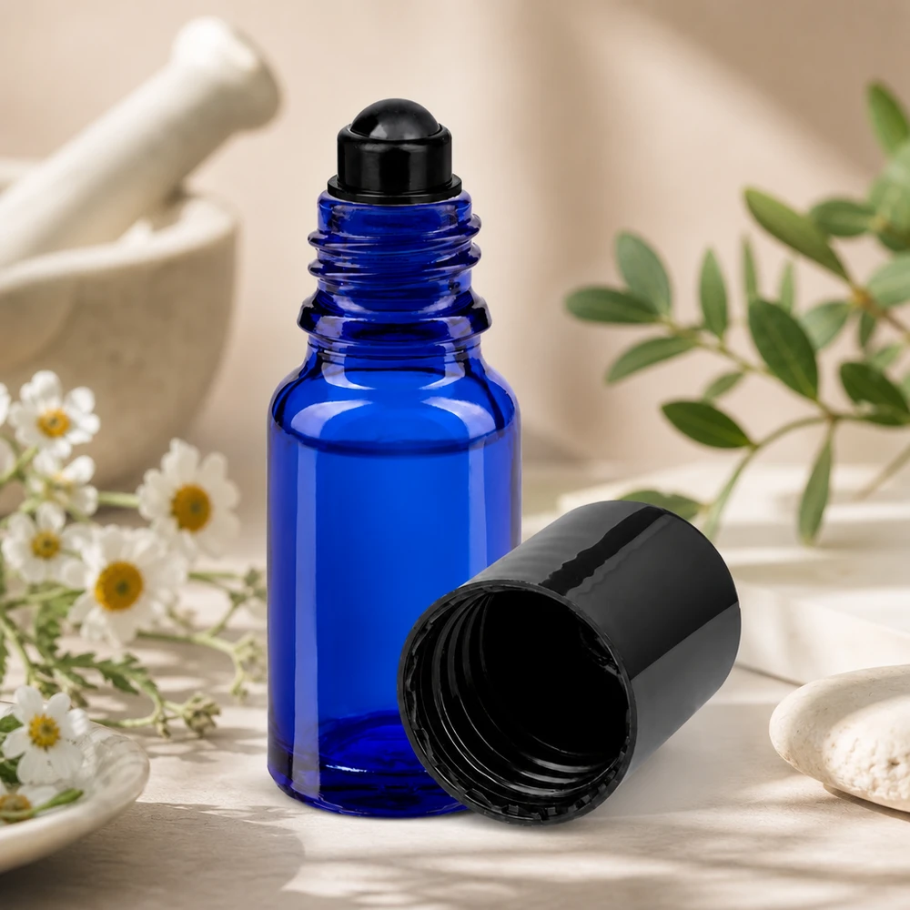 Frasco roll-on azul de 10 ml modelo STD con tapón negro, junto a hierbas de mortero y flores de manzanilla
