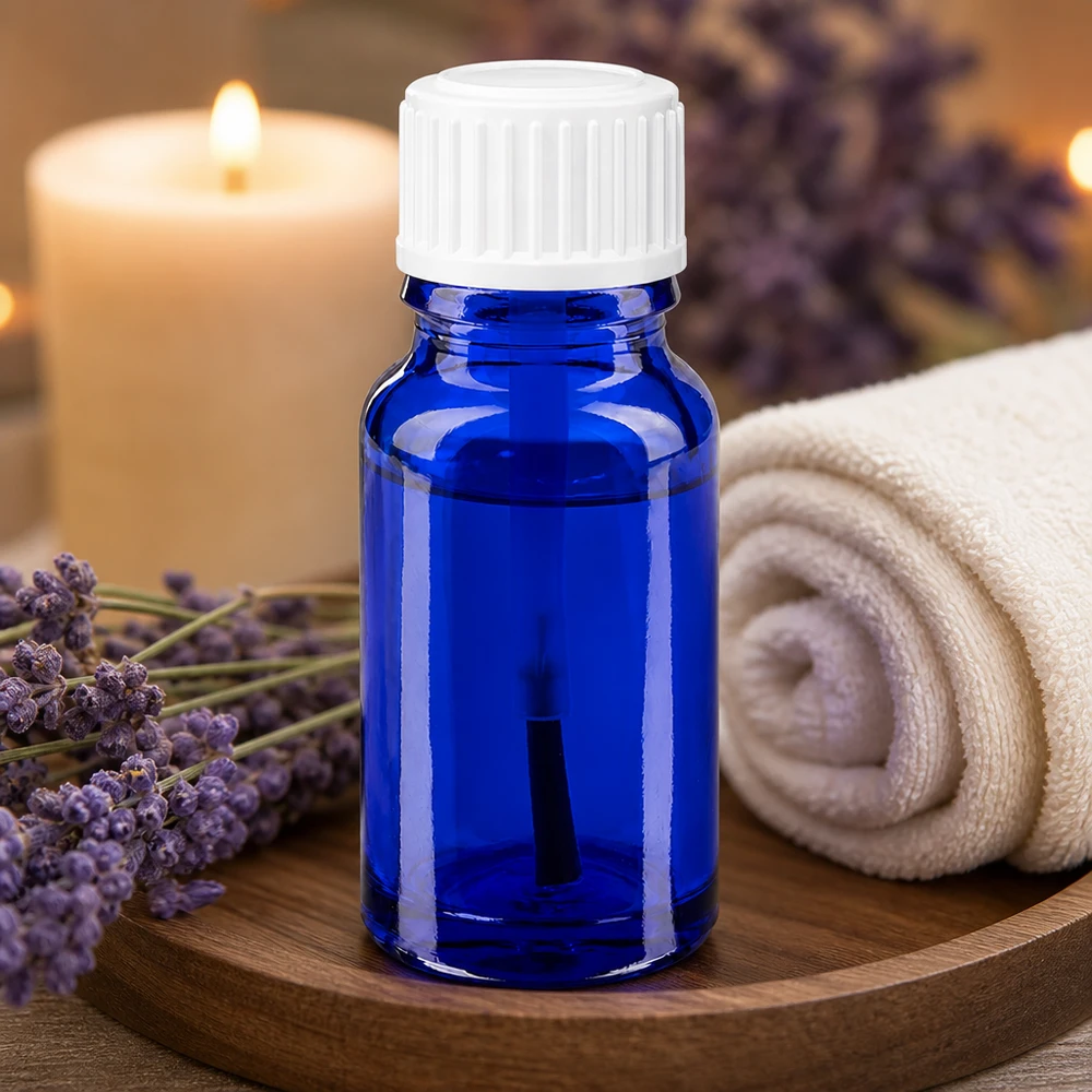 Frasco de aromaterapia de 10 ml, de cristal azul de farmacia con un aplicador de pincel blanco junto a flores de lavanda