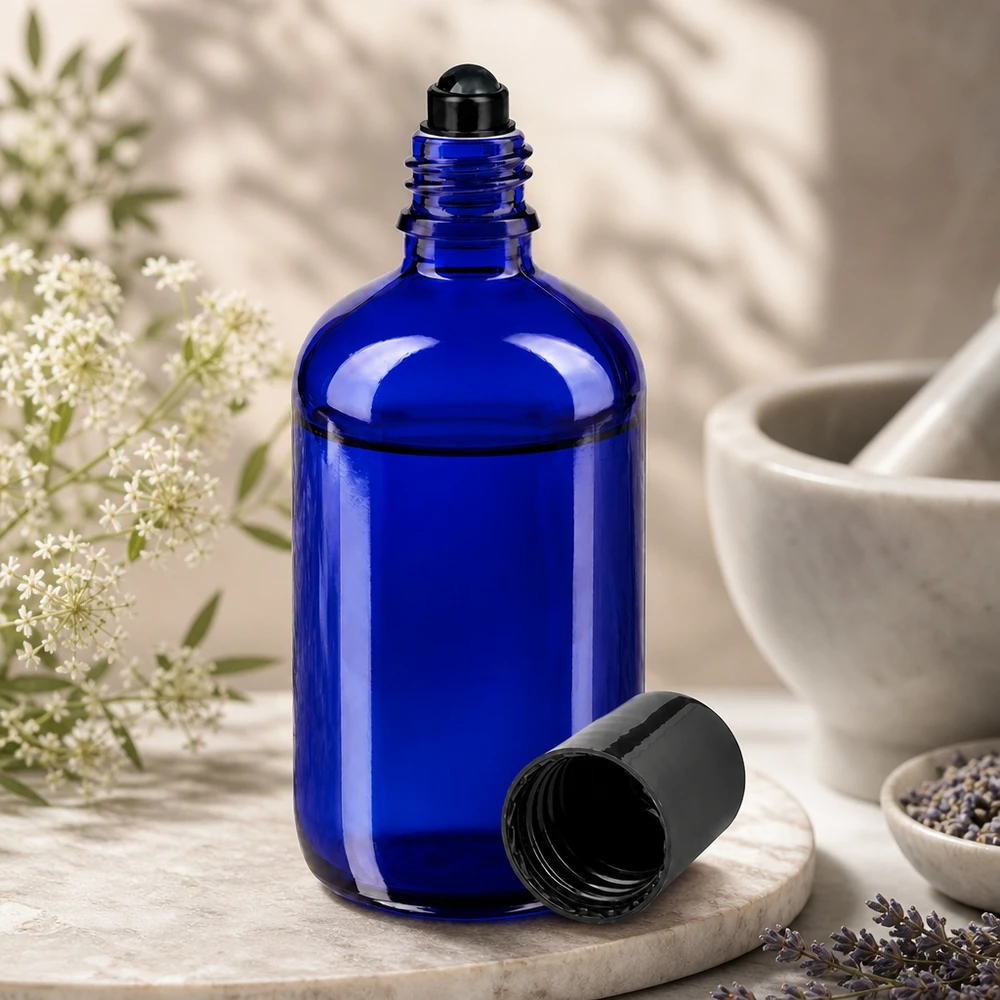 Botella de farmacia azul 100ml roll-on cap negro Botella de cristal azul cobalto de 100 ml con aplicador de bola negra, abierta junto a flores de lavanda y un mortero