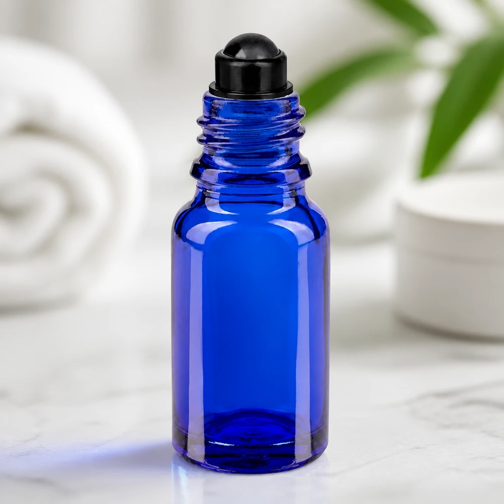 Botella de farmacia azul 10ml tapón roll-on negro Frasco de cristal azul de 10 ml con aplicador de bola negro sobre mármol, sobre un fondo blanco
