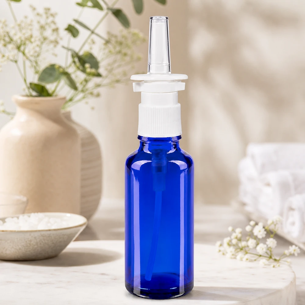 Primer plano de un frasco de spray nasal de 30 ml, de color azul cobalto, con cabezal de bomba de rosca blanco y boquilla de plástico transparente