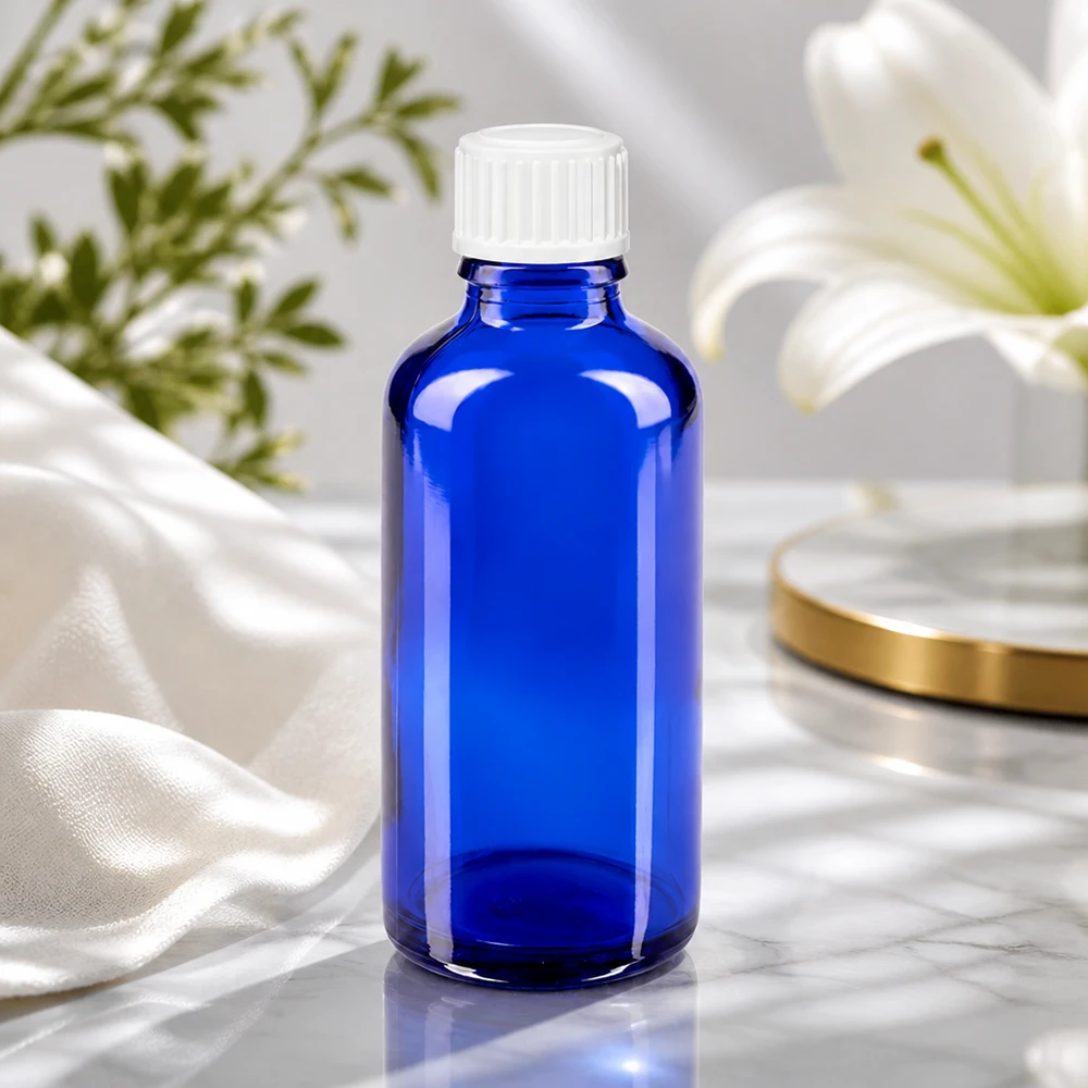 Botella de farmacia azul 50ml tapón de rosca blanco estándar Frasco de cristal azul de 50 ml con tapón de rosca blanco junto a un lirio blanco sobre una superficie de mármol