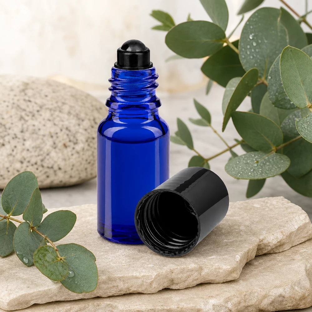 Botella de farmacia azul 10ml tapón roll-on negro Frasco roll-on ApoGlas azul de 10 ml con tapón negro junto a ramas de eucalipto sobre piedra natural
