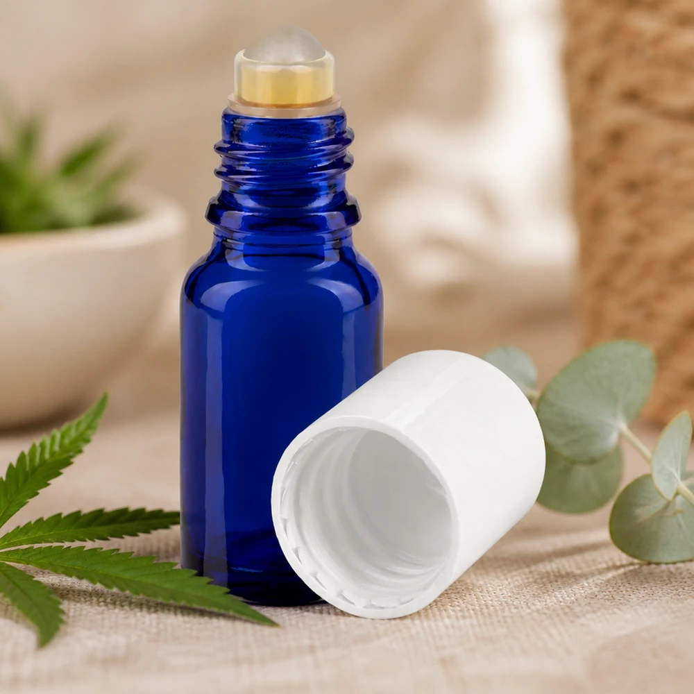 Botella de farmacia azul 10ml tapón roll-on blanco Frasco azul de 10 ml con aplicador de bola y tapón blanco, junto a hojas de cáñamo y eucalipto sobre tela de lino