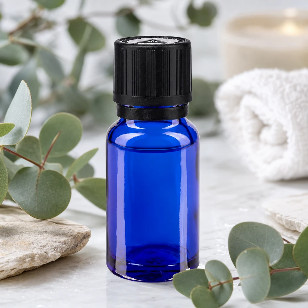 Frasco de farmacia azul cobalto de 10 ml con tapón OV negro sobre fondo de mármol entre ramas de eucalipto