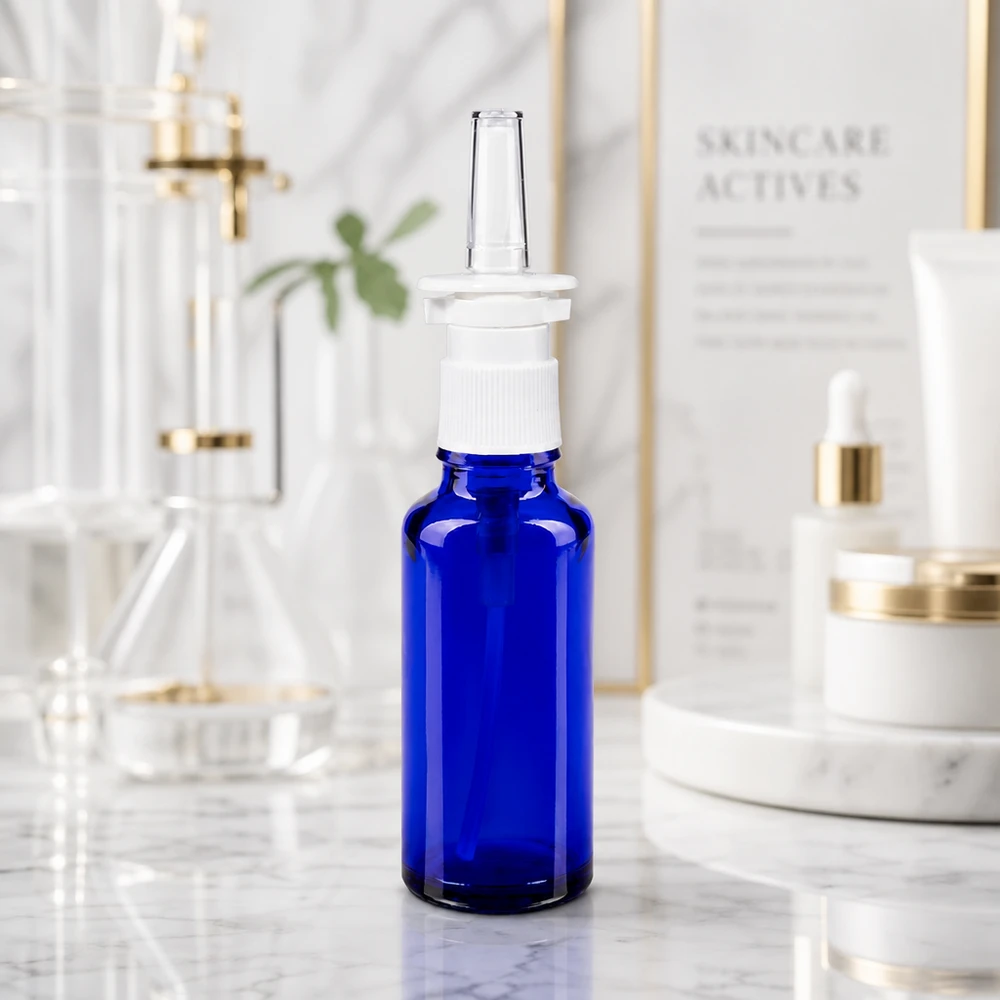 Frasco de cristal azul cobalto de 30 ml con dosificador en forma de pulverizador nasal blanco sobre fondo de mármol