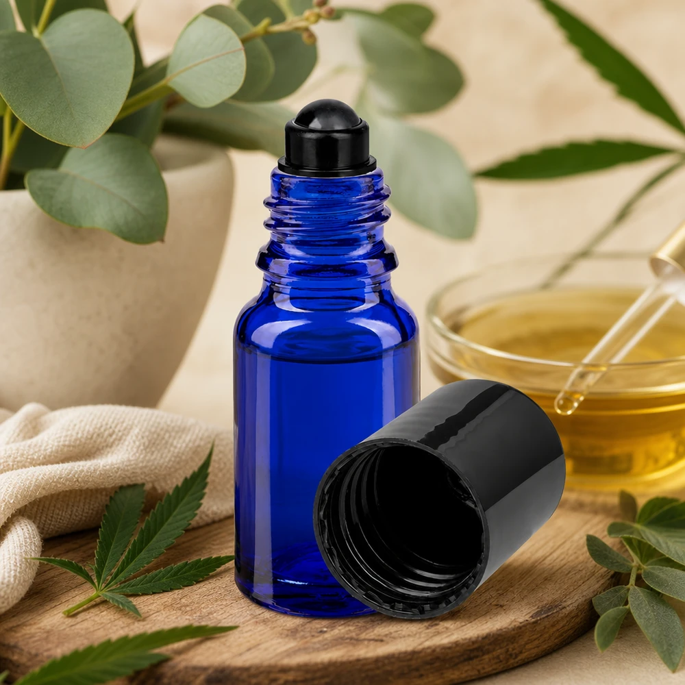 Botella de farmacia azul 10ml tapón roll-on negro Frasco roll-on ApoGlas azul de 10 ml con tapón negro sobre una tabla de madera, junto a una hoja de cannabis y un eucalipto
