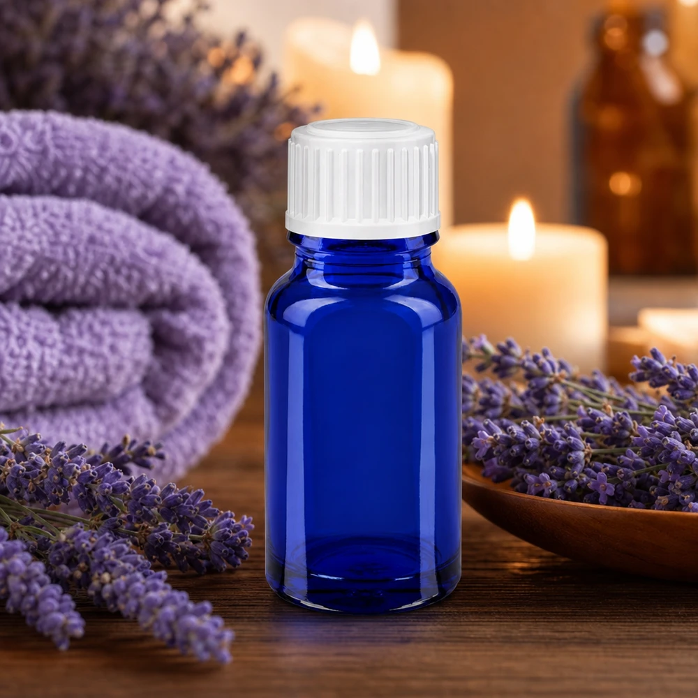 Frasco de cristal azul de 10 ml con tapón blanco, rodeado de flores de lavanda y velas
