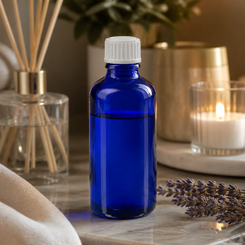 Frasco de cristal azul de 50 ml con tapón cuentagotas sobre mármol, junto a lavanda y un difusor de ambientador