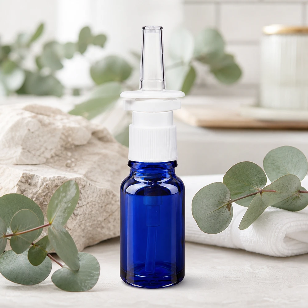Frasco de cristal azul de 10 ml con boquilla transparente para spray nasal, sobre un fondo natural de eucalipto
