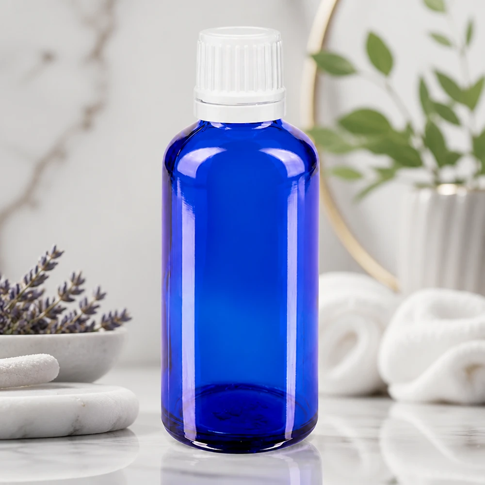 Botella de cristal azul de 50 ml con tapón de rosca blanco sobre mármol, junto a la lavanda