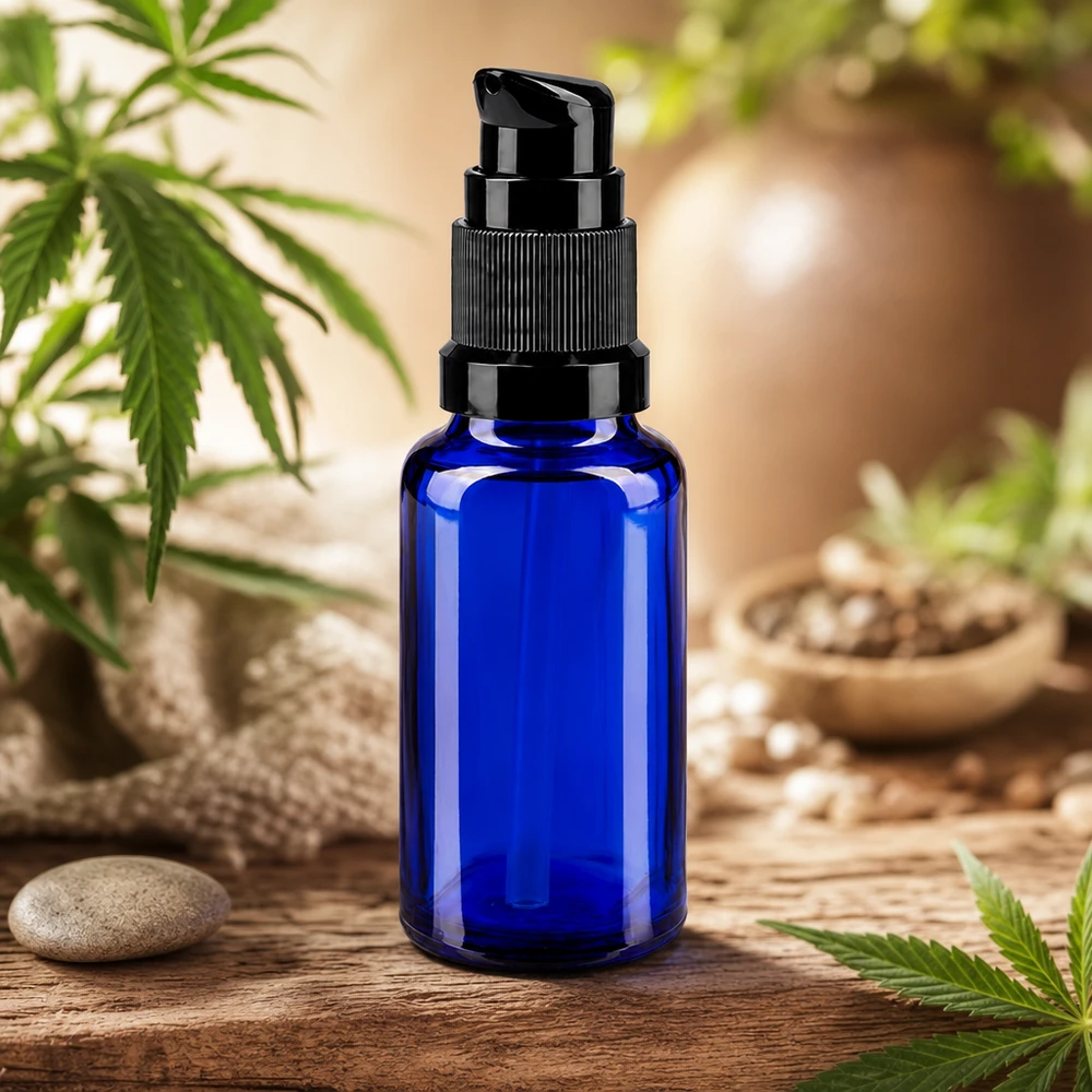 Frasco dosificador de 20 ml de cristal de farmacia de color azul cobalto con cabezal dosificador negro, con plantas de cannabis en el fondo
