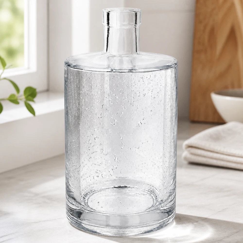 Botella de vidrio de 700 ml «Marie» sin tapón UNiTWIST® Elegante 700ml Glasflasche Marie mit Luftbläschen-Optik in modernem Wohnambiente neben Handtüchern und Holzschale