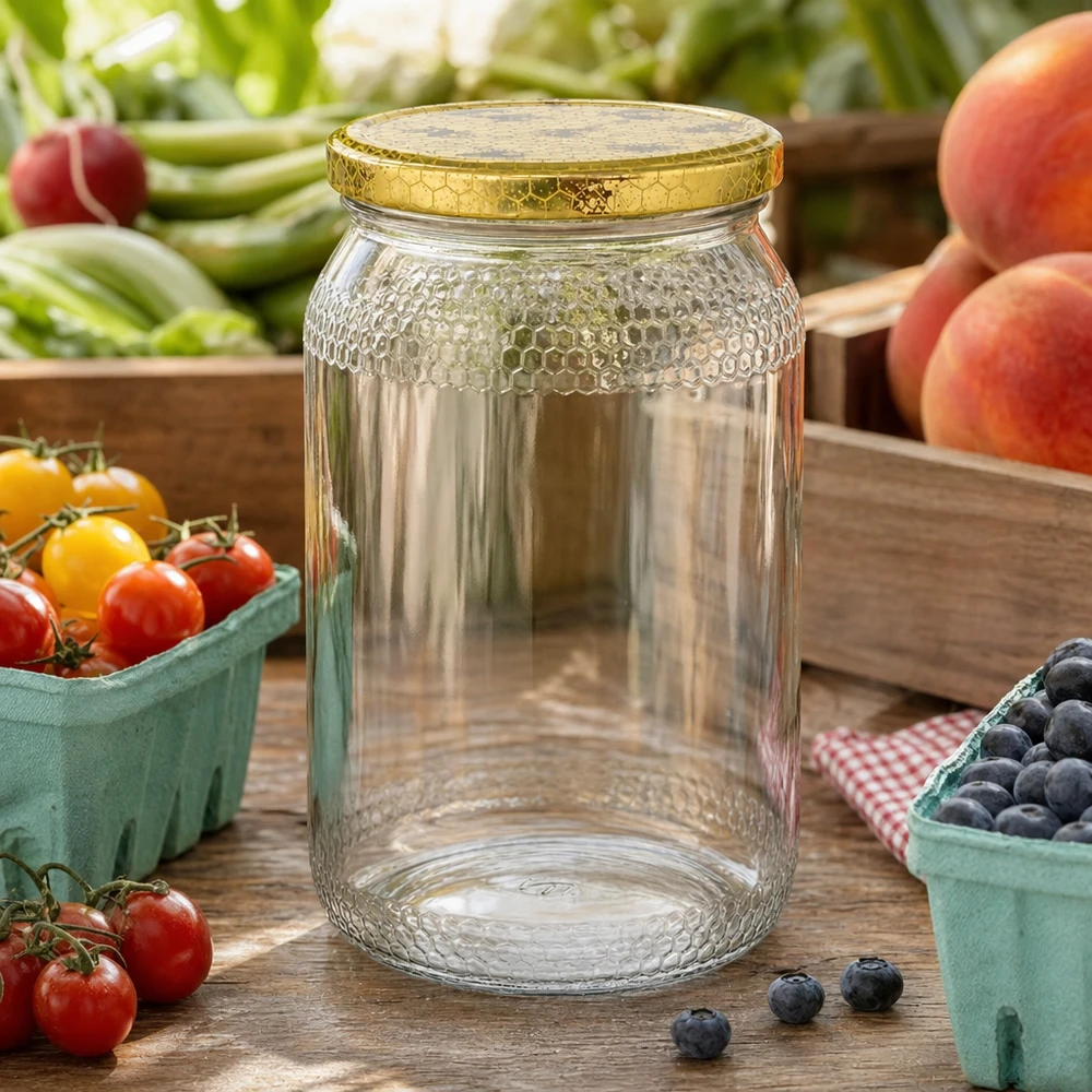 Tarro de miel de 900 ml vacío con tapa de panal dorada entre frutas y verduras frescas sobre mesa de cocina de madera