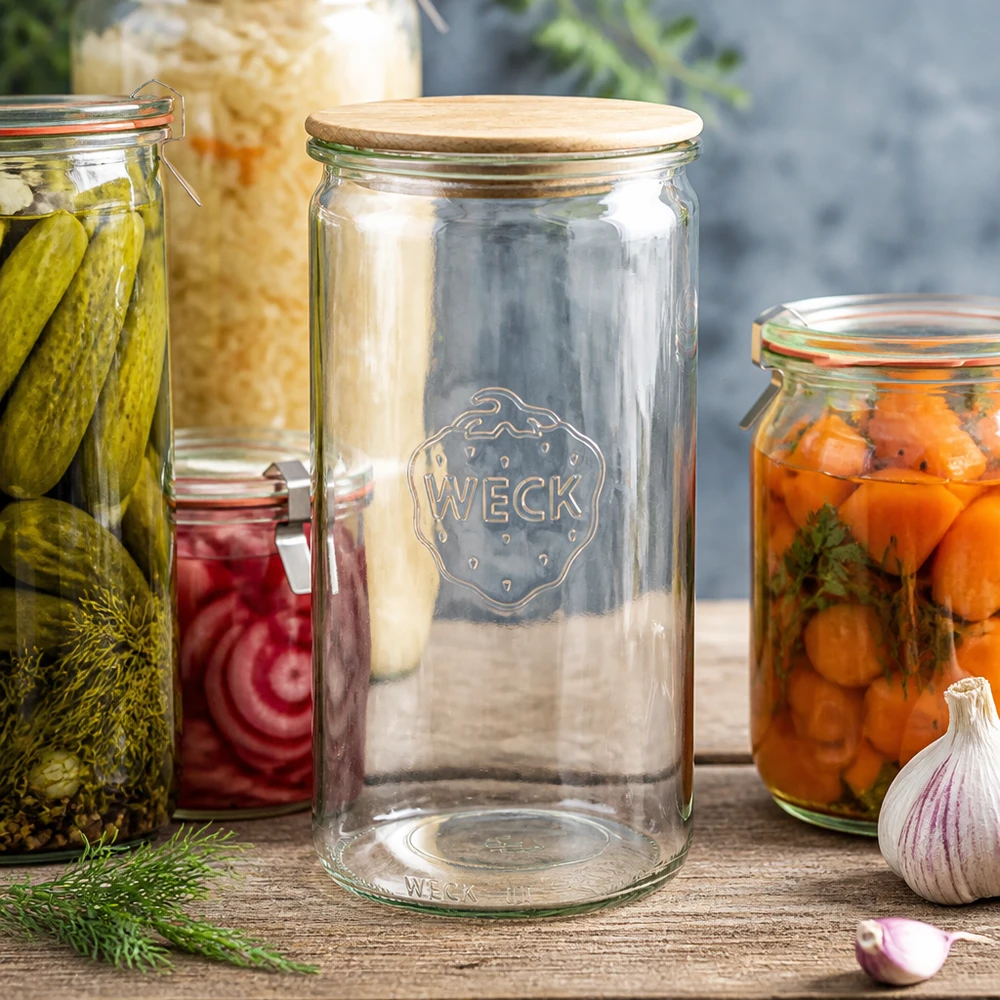 Tarro cilíndrico WECK RR100 de 1590ml con tapa de madera WECK Zylinderglas 1590ml RR100 mit Holzdeckel zwischen Einmachgläsern mit Gurken Karotten und Sauerkraut auf Holztisch