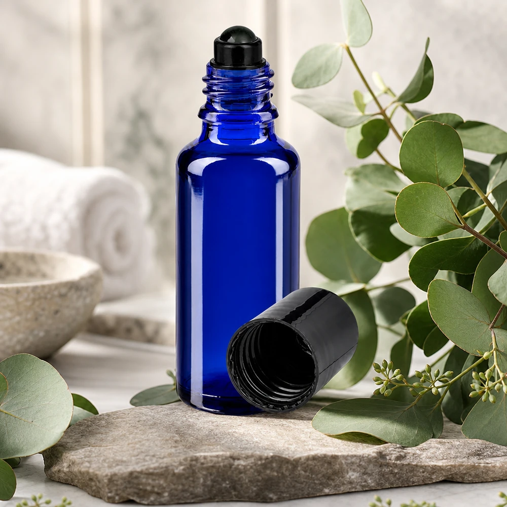 Botella de farmacia azul 30ml tapón roll-on negro Frasco de cristal azul cobalto de 30 ml con aplicador de bola negro sobre una piedra natural entre ramas de eucalipto