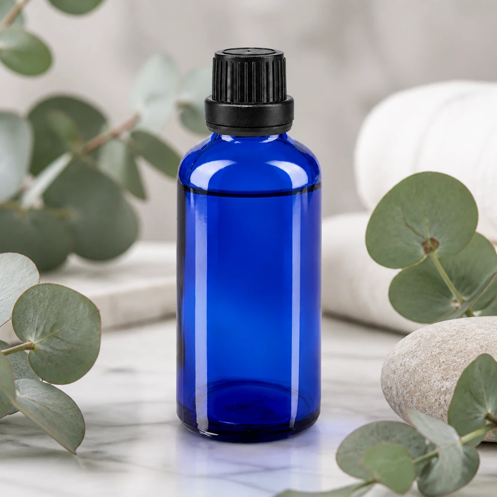 Frasco de cristal de farmacia azul cobalto de 50 ml con tapón de seguridad para niños negro, delante de unas ramas de eucalipto