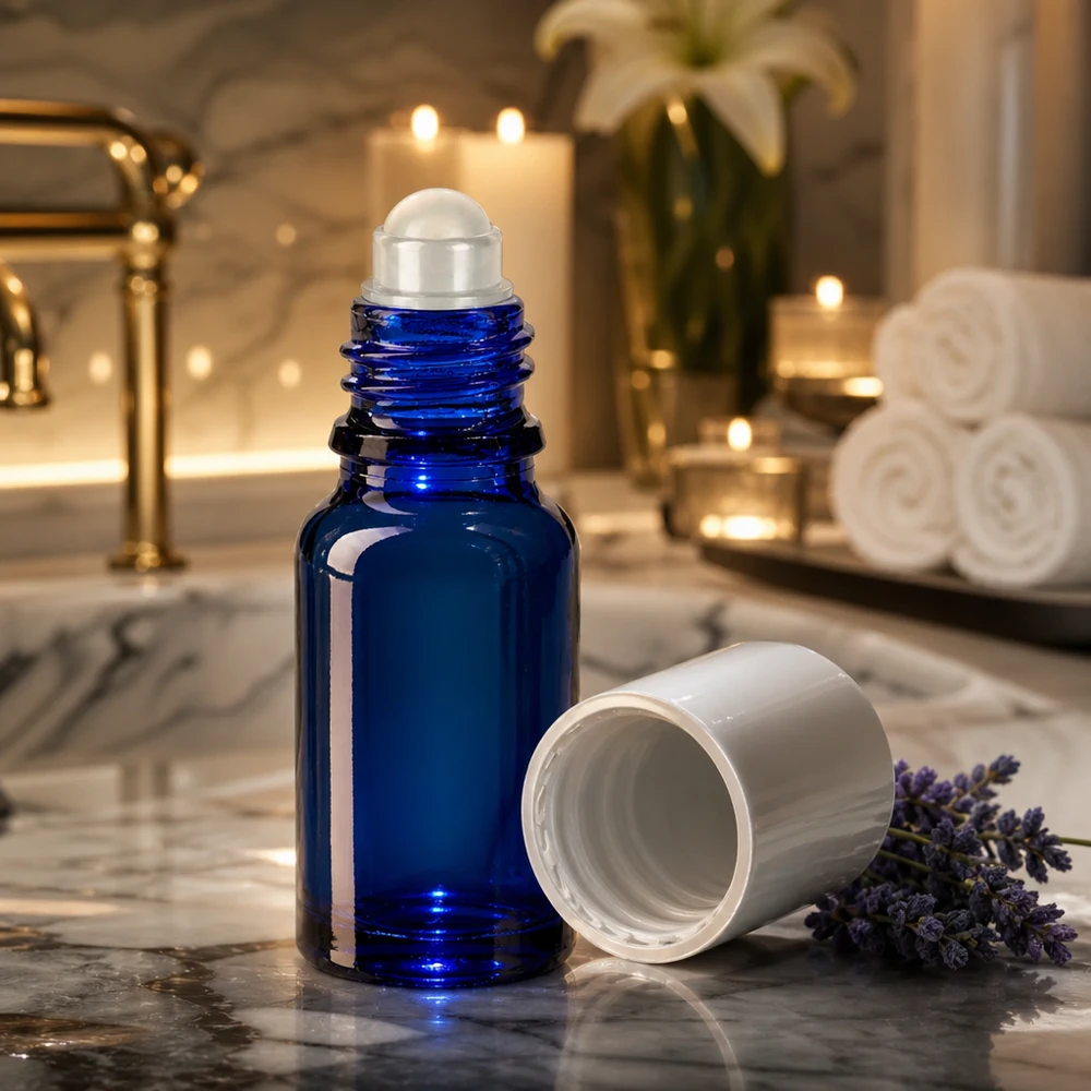 Botella de farmacia azul 10ml tapón roll-on blanco Frasco roll-on azul cobalto de 10 ml con aplicador de bola rodante sobre una superficie de mármol, junto a flores de lavanda