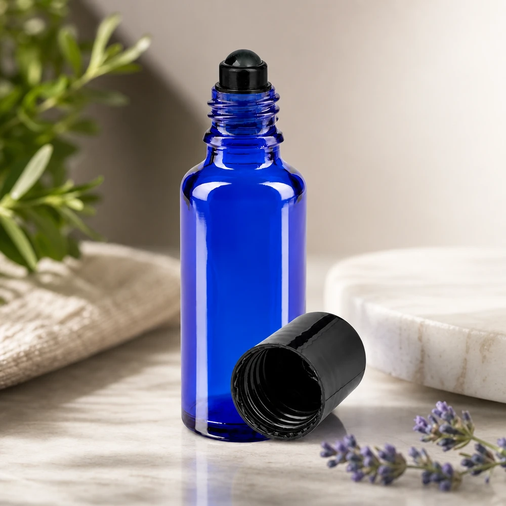 Botella de farmacia azul 30ml tapón roll-on negro Frasco de cristal azul cobalto de 30 ml con aplicador de bola y tapón negro, junto a una ramita de lavanda y otra de romero
