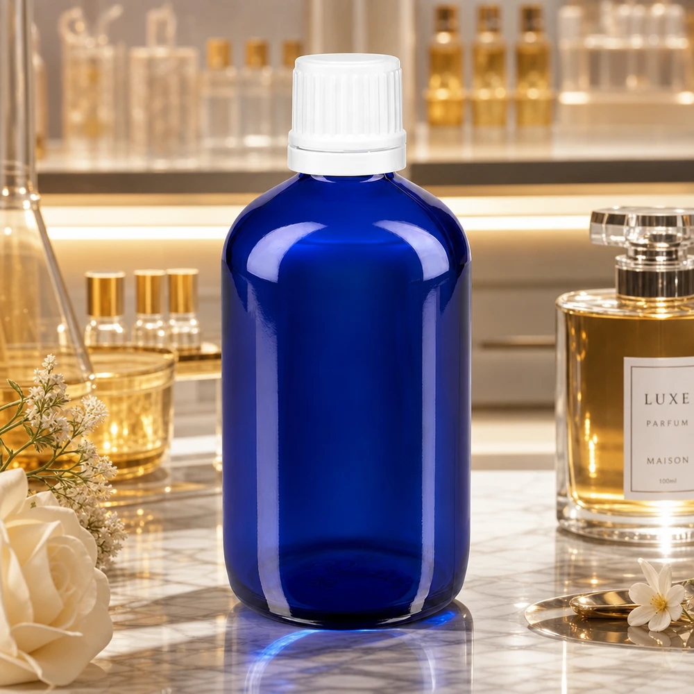 Botella de farmacia azul 100ml tapón de rosca blanco cierre inviolable Frasco de farmacia de cristal azul de 100 ml con tapón OV blanco de 11 mm sobre mármol, junto a un perfume de lujo