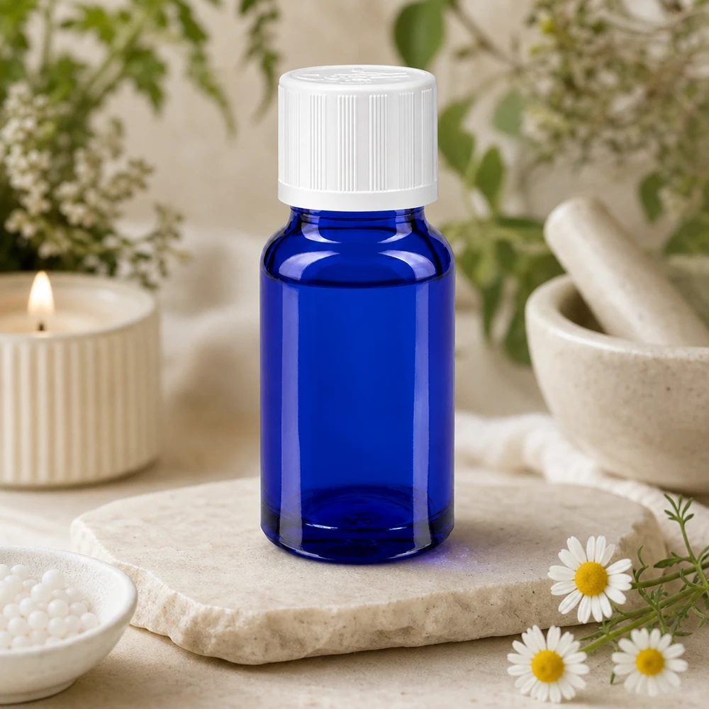 Frasco de farmacia azul de 10 ml con tapón blanco de KiSi sobre una losa de piedra, junto a unas flores de manzanilla