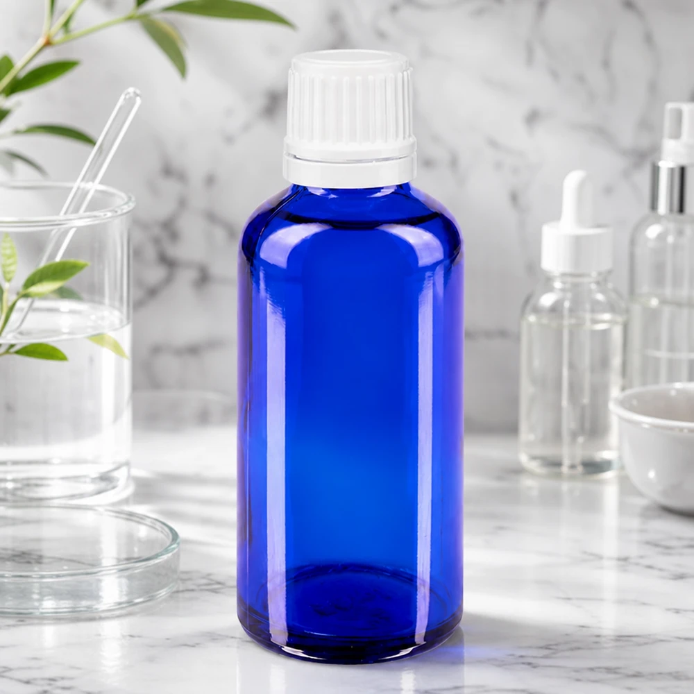Botella de farmacia azul 50ml tapón cuentagotas 1,2mm blanco cierre inviolable Pequeña botella de cristal azul con tapón cuentagotas sobre una superficie de mármol, rodeada de utensilios de laboratorio y plantas
