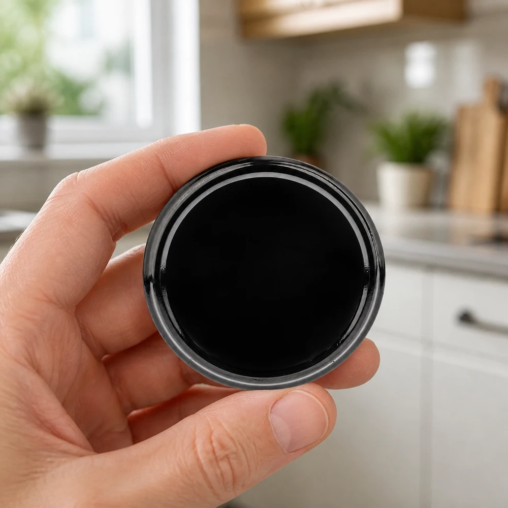 Mano sujetando una tapa BasicSeal de 82 mm, negra, modelo TO82 UNiTWIST, en la cocina