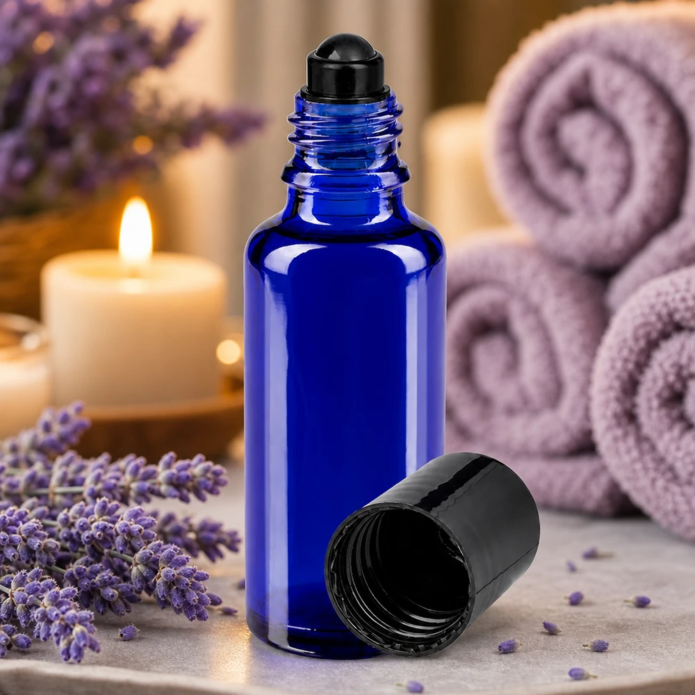 Frasco con aplicador de bola de 30 ml de color azul cobalto, de cristal de farmacia, con tapón negro, junto a flores de lavanda y velas