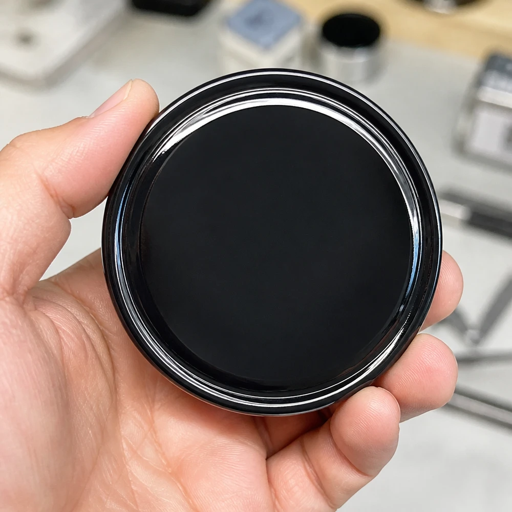 Primer plano de una tapa de rosca BasicSeal de 70 mm, modelo TO70 UNiTWIST, de color negro brillante, en la palma de la mano