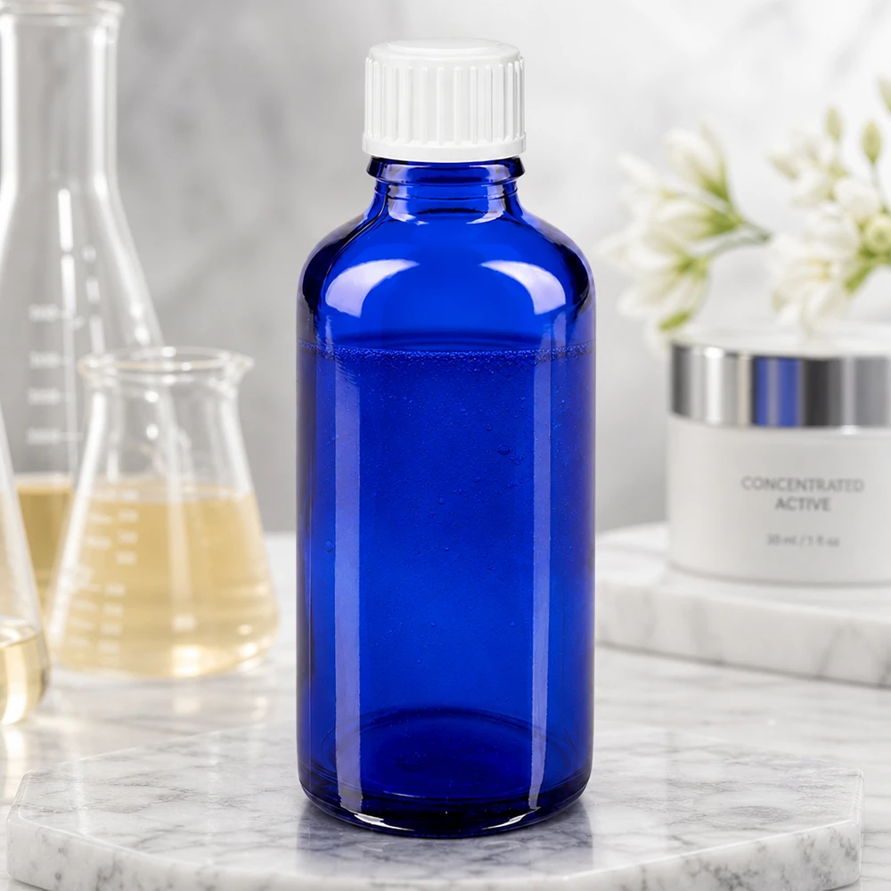 Frasco de cristal azul cobalto de 50 ml con tapón de rosca blanco, junto a un matraz de laboratorio y una crema para el cuidado de la piel