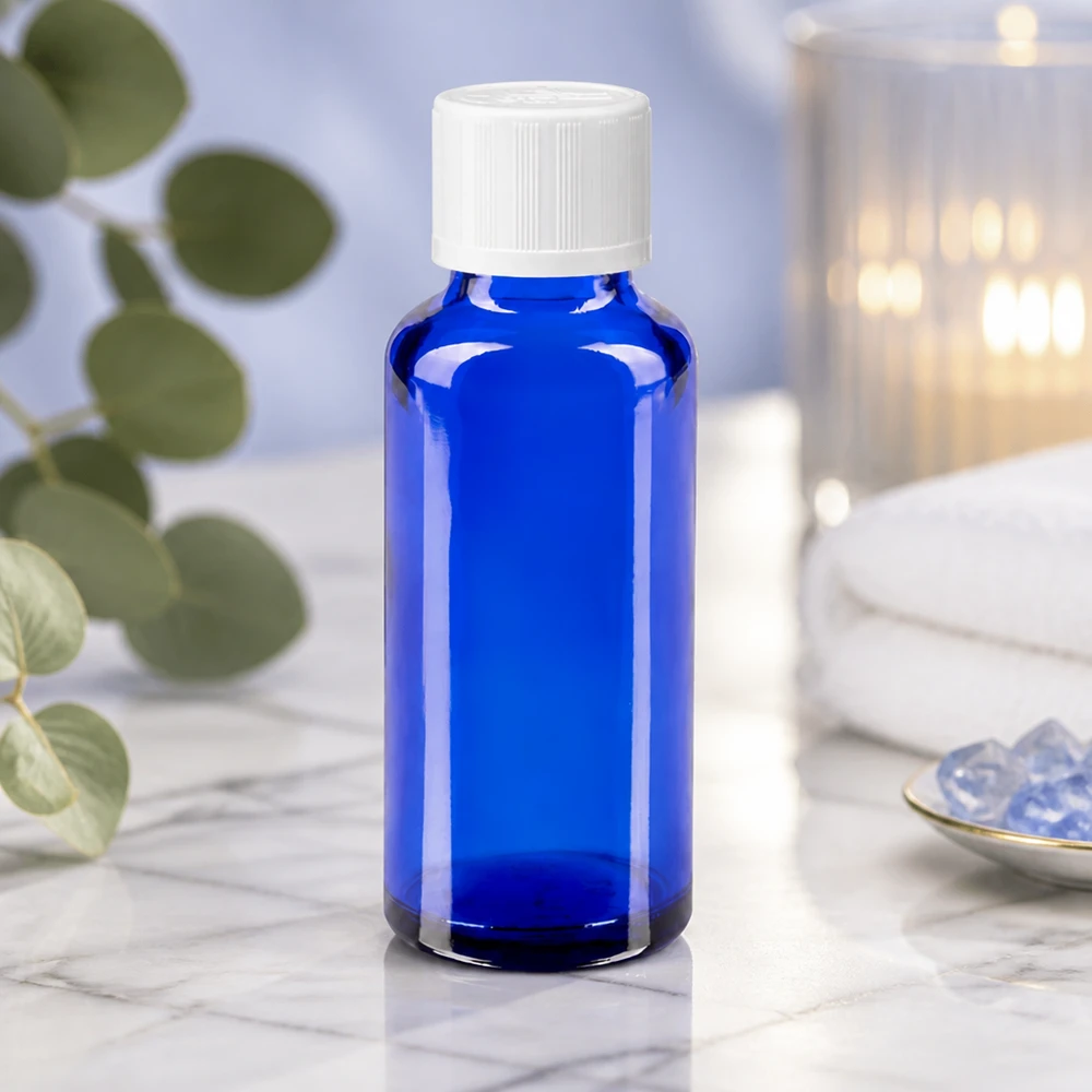 Frasco azul de farmacia de 30 ml con tapón de rosca blanco sobre mármol blanco, junto a unos cristales y una vela