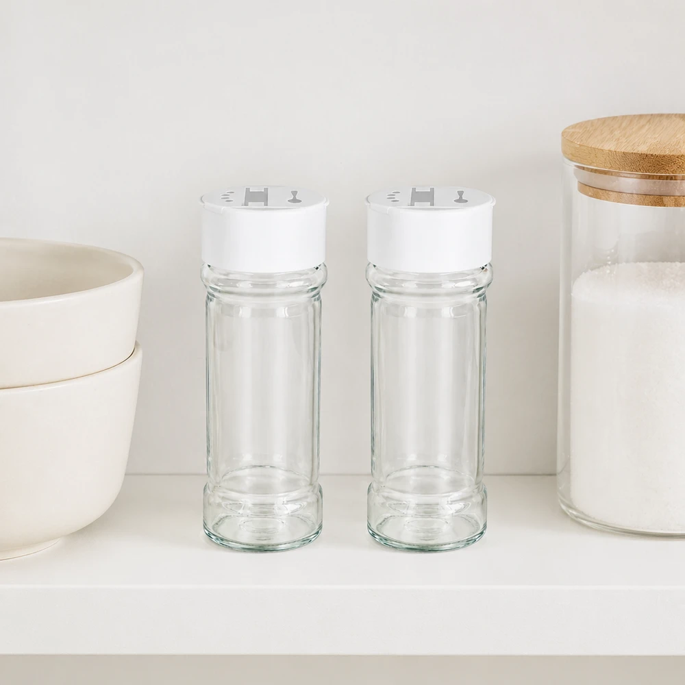 Dos tarros para especias de 100 ml con tapa blanca de doble dosificador, colocados uno al lado del otro en una estantería blanca