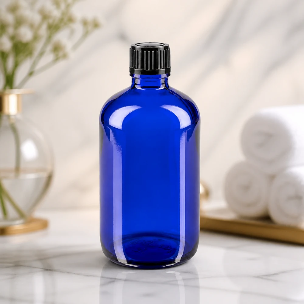 Frasco cilíndrico de cristal azul de 100 ml con tapón de rosca negro estriado sobre una superficie de mármol