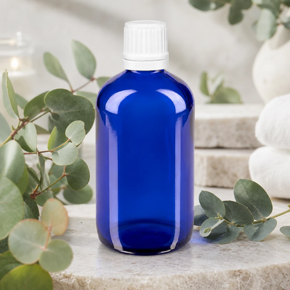 Botella de farmacia azul 100ml tapón de rosca blanco cierre inviolable Frasco de farmacia azul cobalto de 100 ml con tapón de seguridad blanco, sobre una piedra natural con ramitas de eucalipto