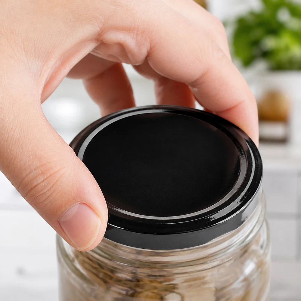 Se coloca la tapa negra TO63 en un tarro de conserva con alimentos. Se muestra a mano cómo se cierra.