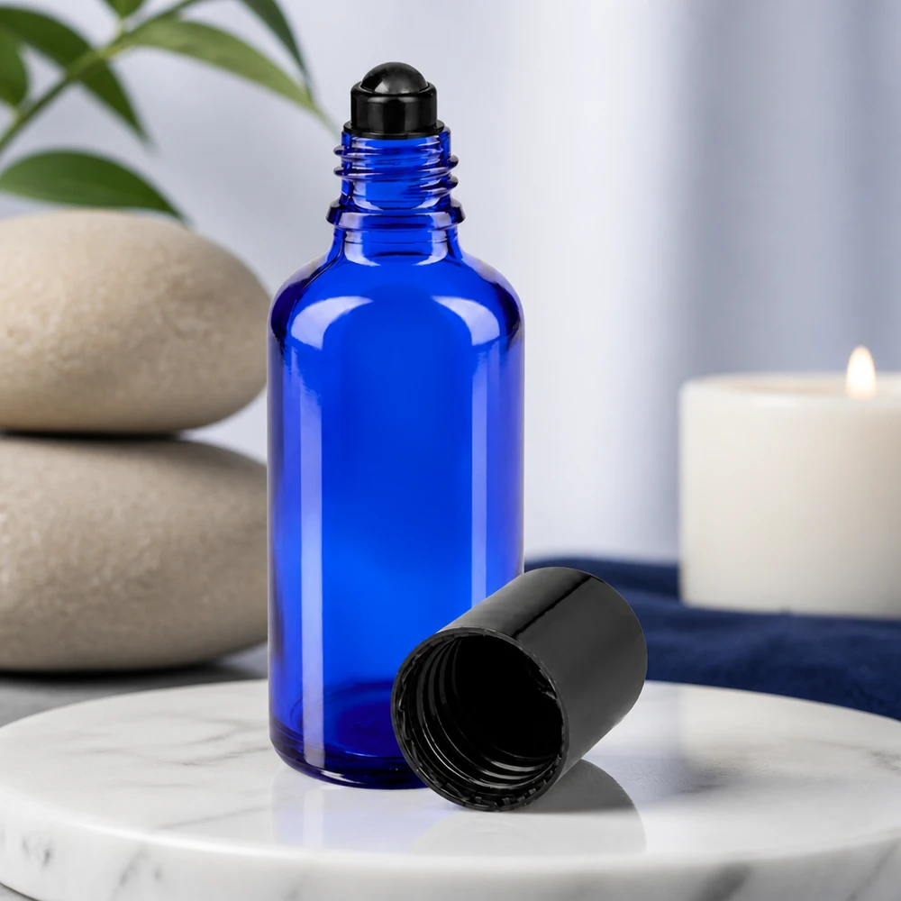 Frasco de cristal azul de 50 ml con aplicador de bola negro y tapón retirado, sobre una superficie de mármol