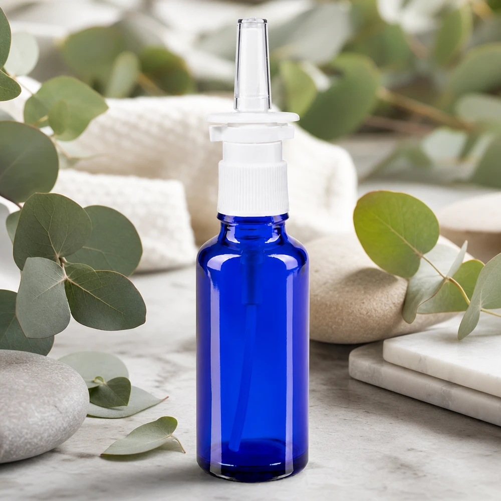 Frasco de spray nasal de 30 ml, de color azul cobalto, con cabezal dosificador blanco y ramitas de eucalipto como decoración natural