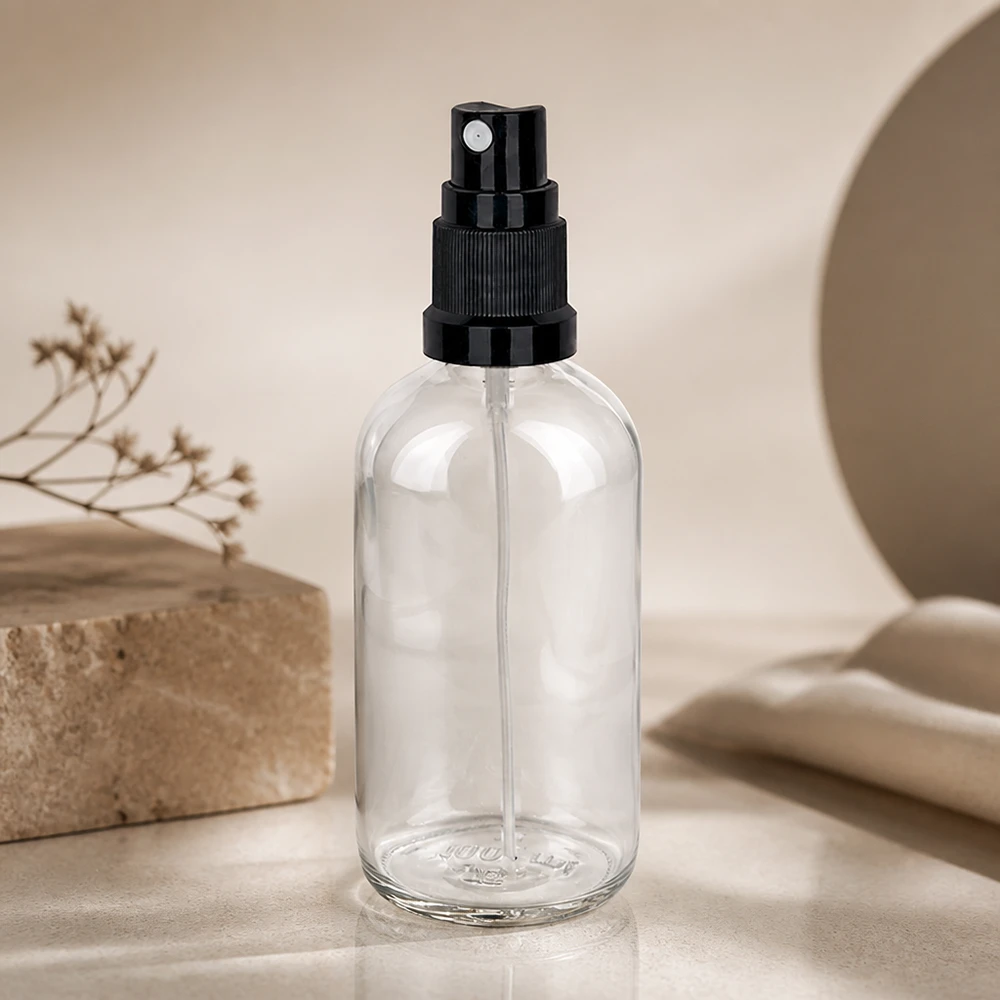 Botella pulverizadora de 100 ml de diseño minimalista, de cristal transparente con pulverizador negro sobre fondo de mármol