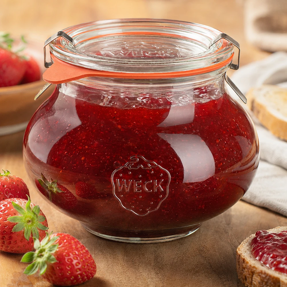 Frasco decorativo de 560 ml, completo, WECK RR80 Tarro decorativo WECK de 560 ml lleno de mermelada de fresa casera, tapa basculante cerrada, rodeado de frutas y verduras frescas.