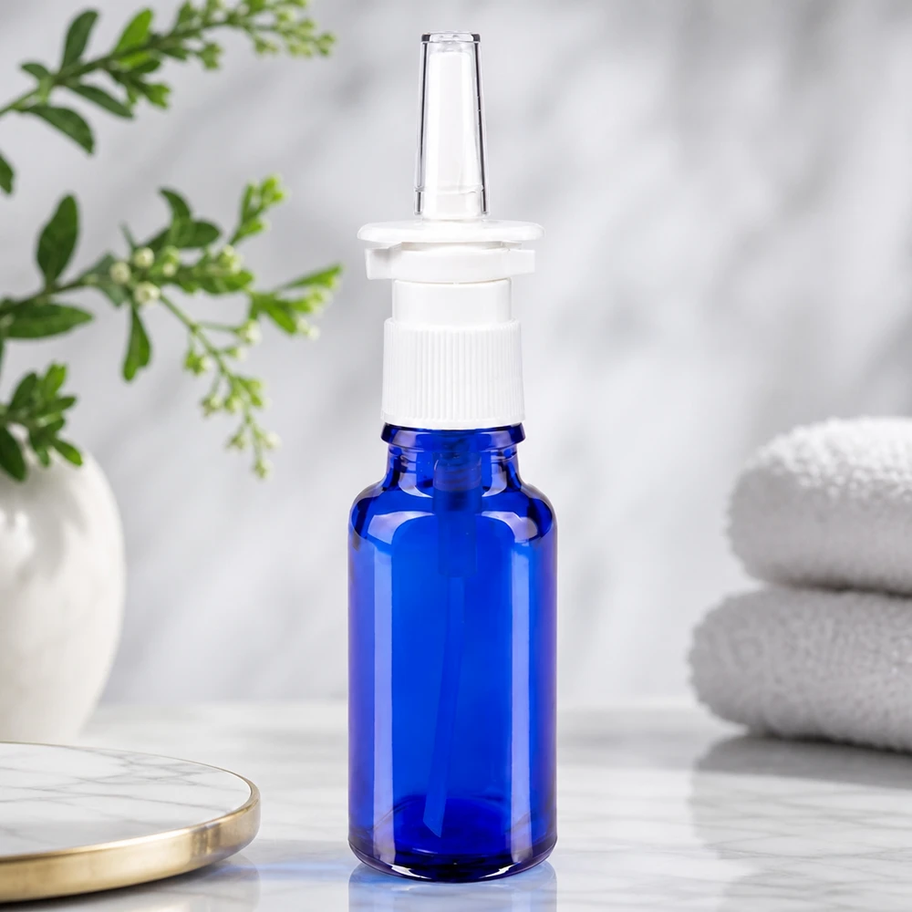 Frasco de farmacia azul de 20 ml con boquilla transparente para spray nasal y cabezal de presión blanco sobre fondo de mármol