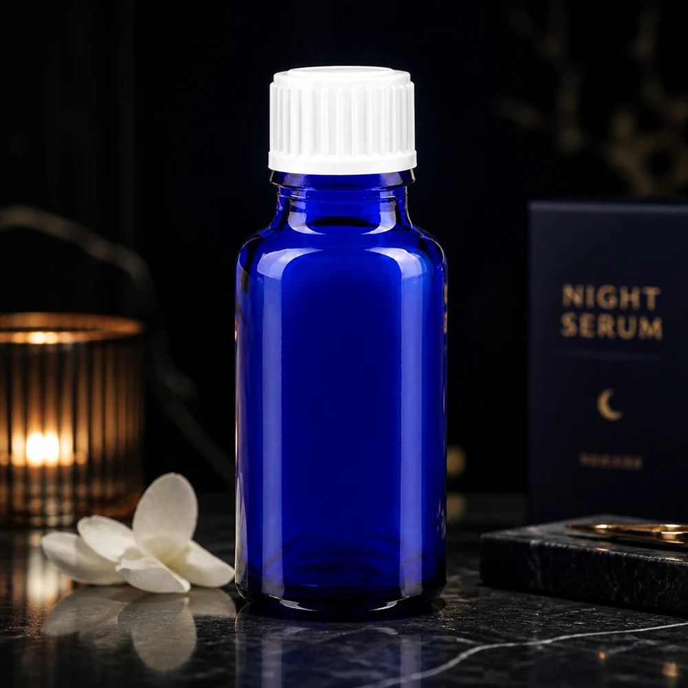 Frasco de cristal azul cobalto de 20 ml con tapón blanco junto al envase del sérum de noche sobre un fondo oscuro