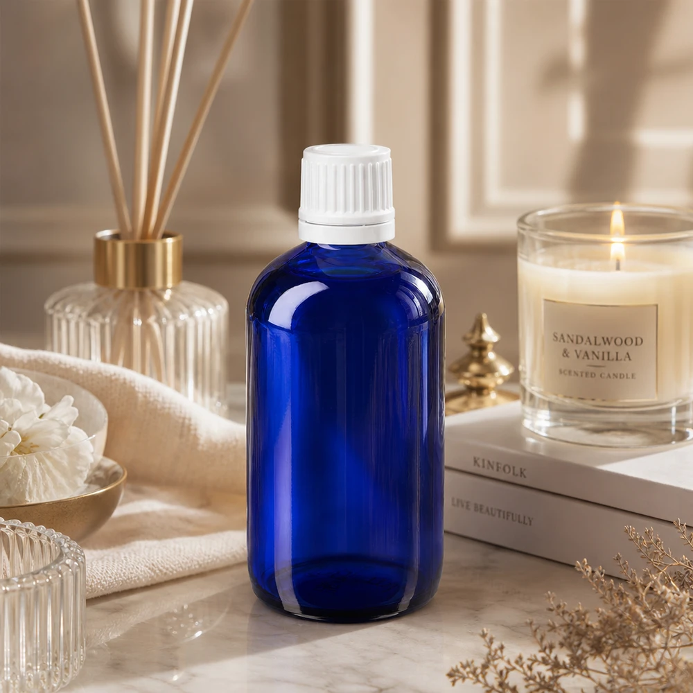 Botella de farmacia azul 100ml tapón de rosca blanco cierre inviolable Frasco de farmacia azul de cristal de 100 ml con tapón blanco a prueba de niños, sobre mármol junto a una vela de sándalo