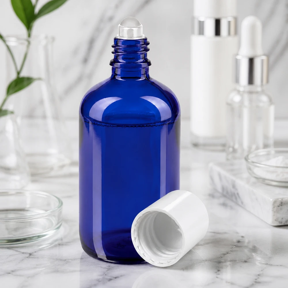 Botella de farmacia azul 100ml tapón roll-on blanco Botella de cristal azul de 100 ml con aplicador de bola y tapón blanco sobre una superficie de mármol